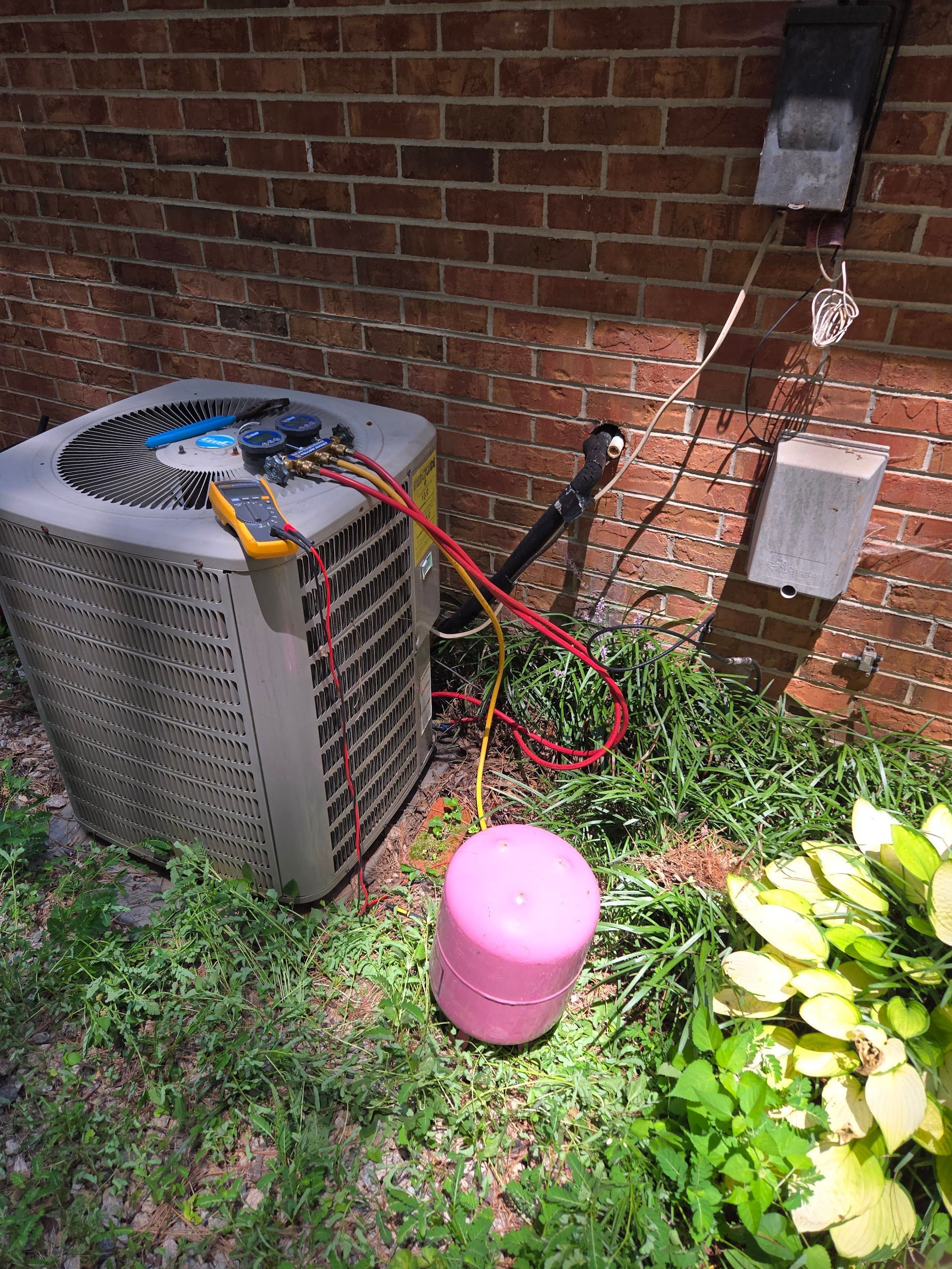 An air conditioner is being serviced outside of a brick building.