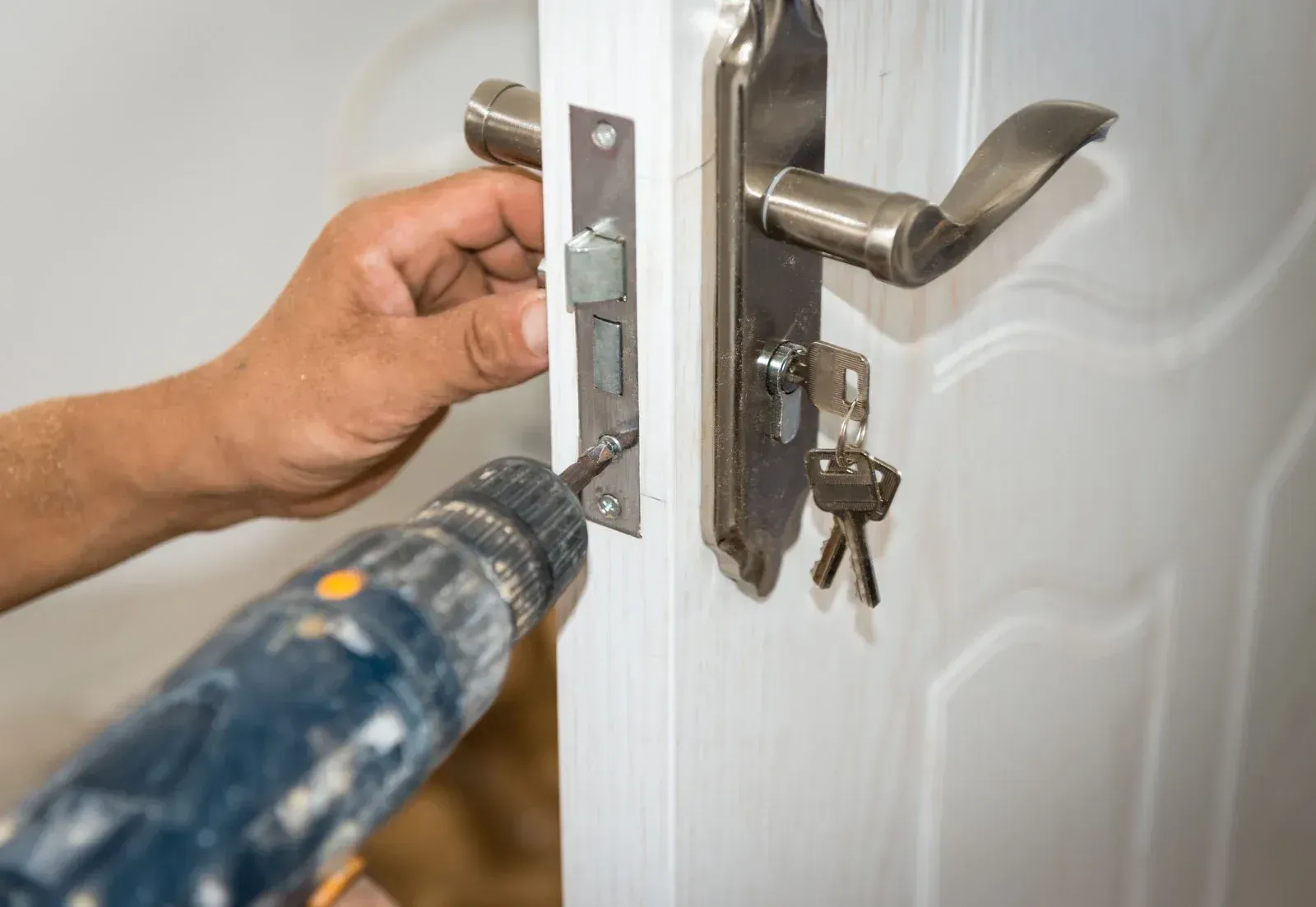 A person is installing a door lock with a drill.