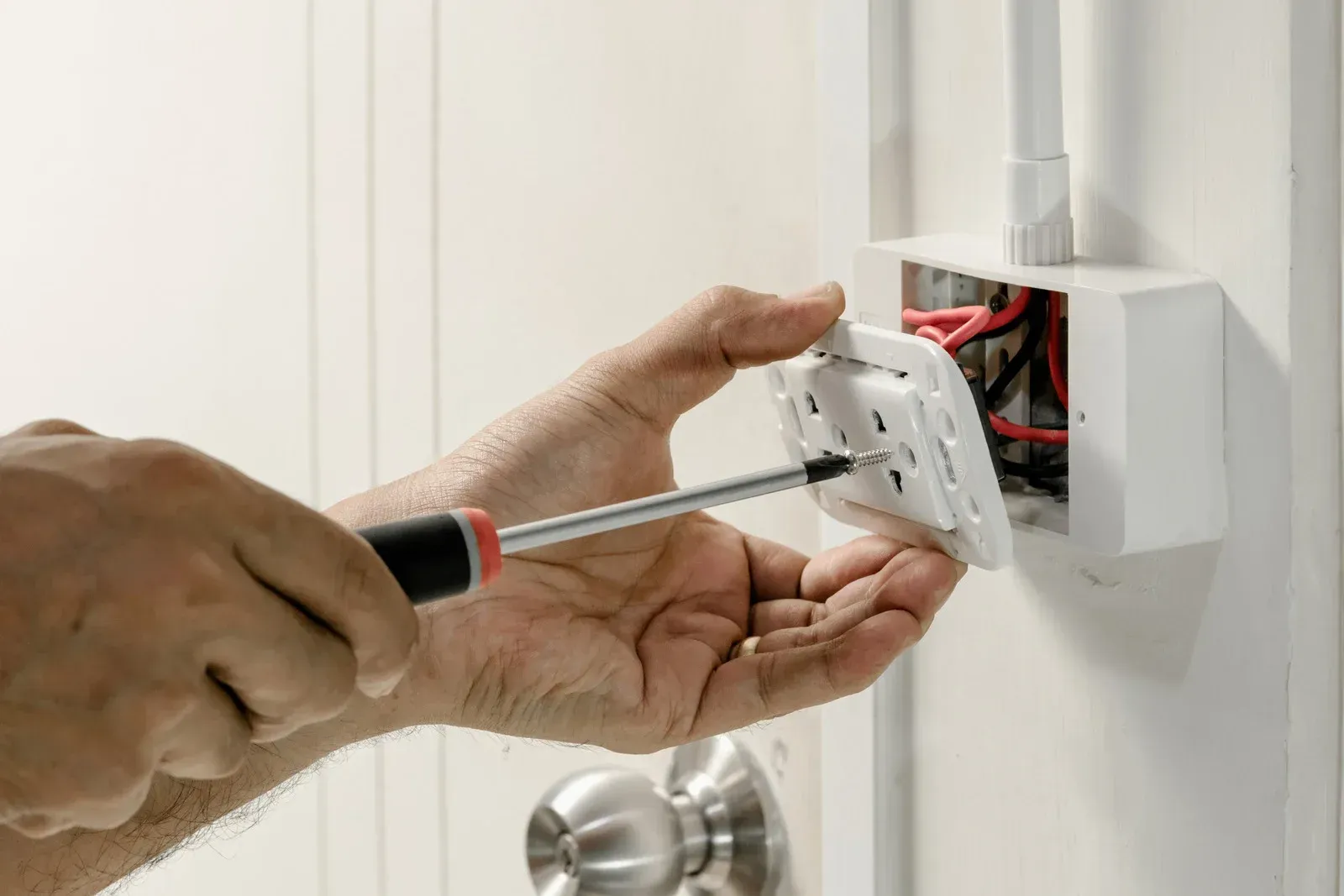 A person is fixing an electrical outlet with a screwdriver.