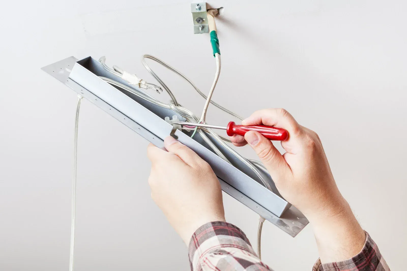 A person is fixing a light fixture with a screwdriver.