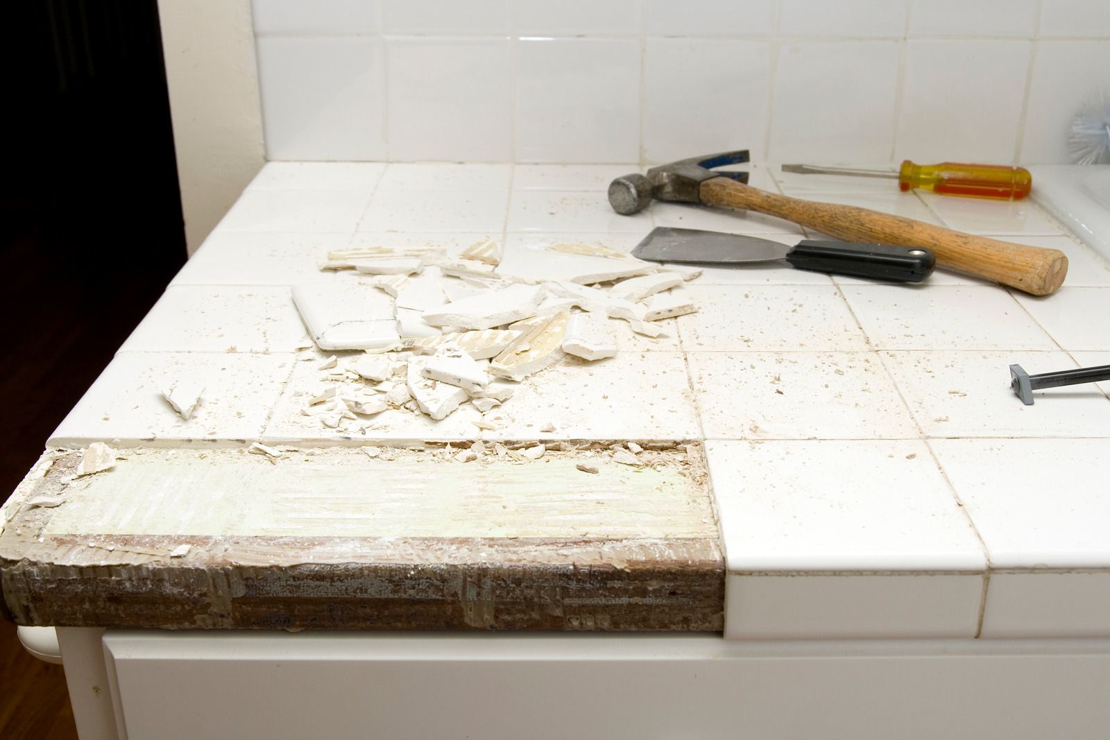 A hammer , spatula , and screwdriver are on a kitchen counter.