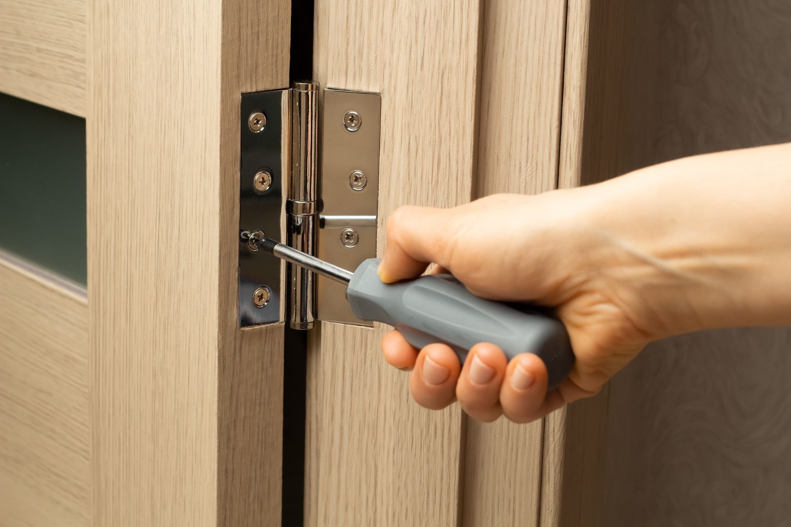 A person is fixing a door knob with a screwdriver.