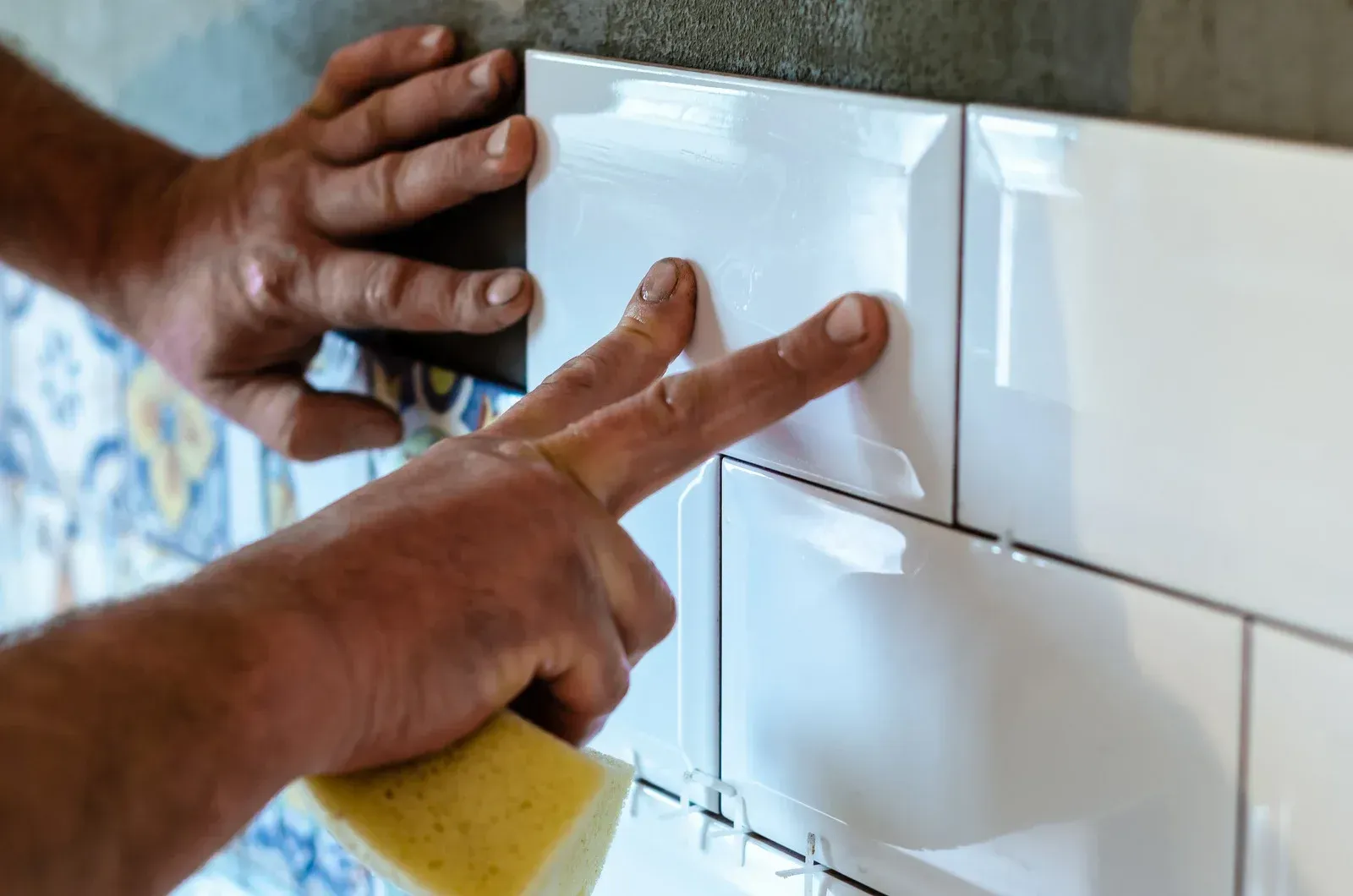 A man is installing tiles on a wall with a sponge.