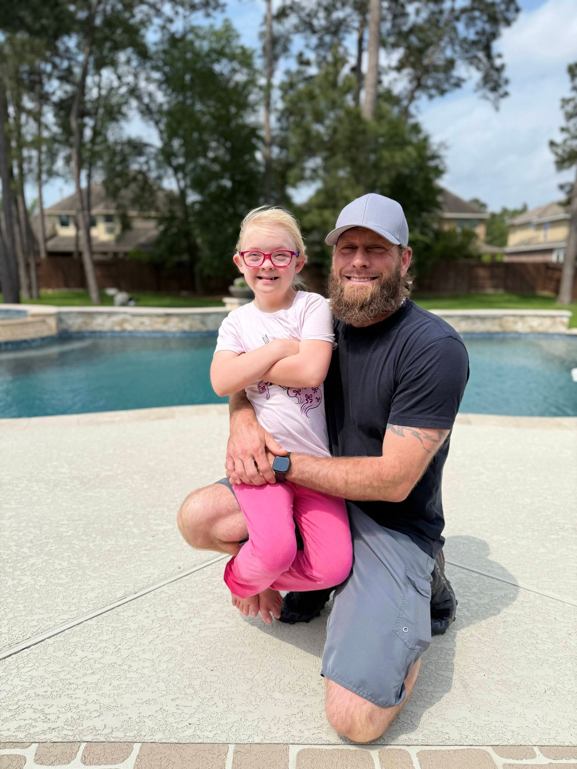 A man and a little girl are posing for a picture in front of a pool.