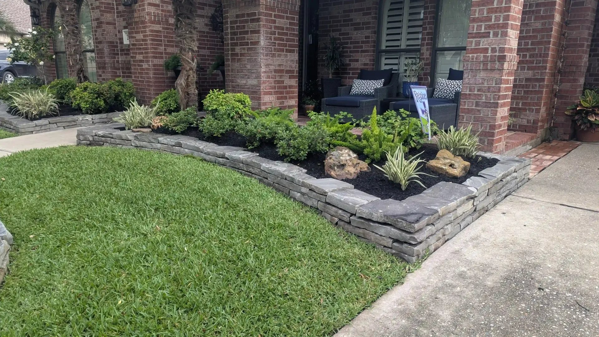 A brick house with a lush green lawn and a stone wall in front of it.