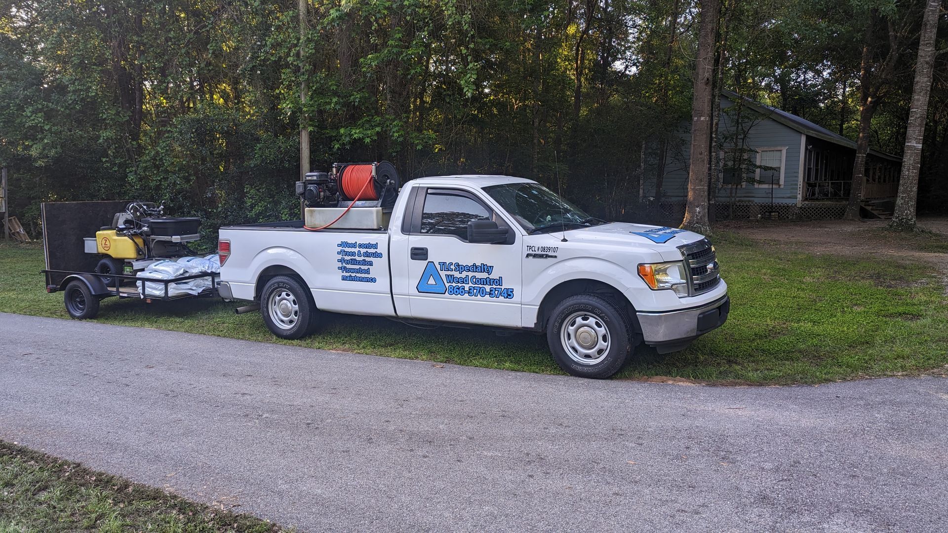 A white truck with a trailer attached to it is parked on the side of the road.