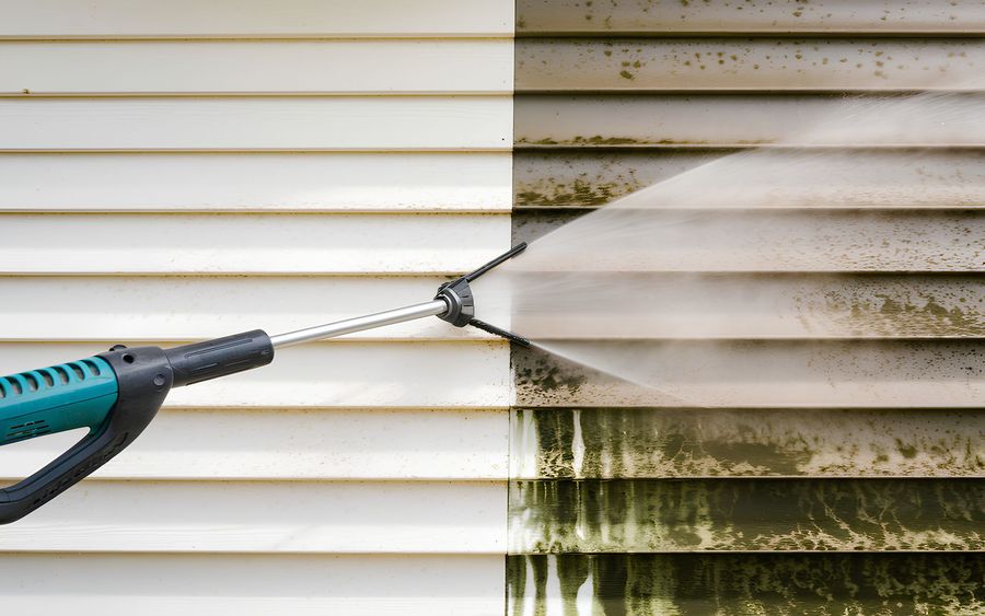 A person is cleaning a house with a high pressure washer.