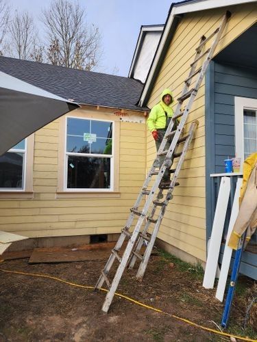 A man is standing on a ladder on the side of a house.