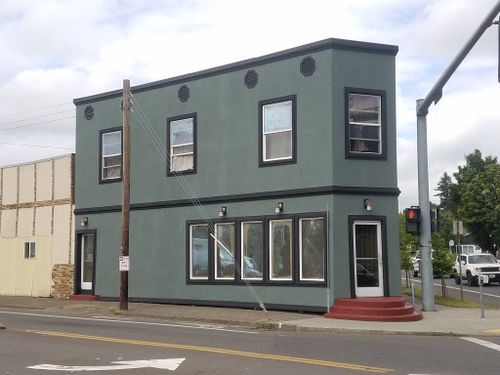 A green building with a lot of windows is on the corner of a street.
