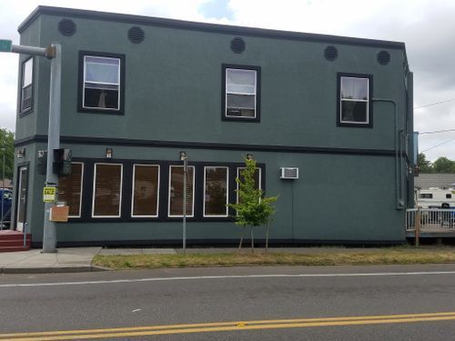 A green building with a lot of windows is on the corner of a street