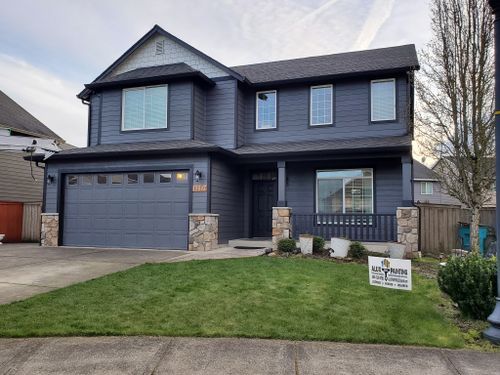 A large house with a gray garage door and a sign in front of it.