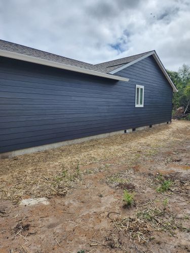 A blue house with a white window is sitting in the middle of a dirt field.