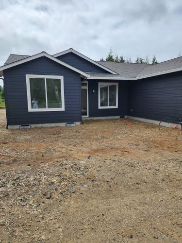 A blue house with white windows is sitting on top of a dirt field.