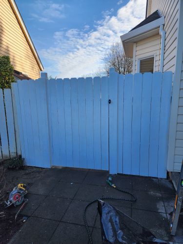 A white wooden fence is being painted in front of a house.