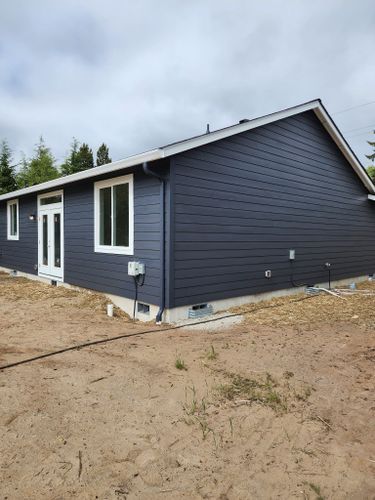 A blue house with white windows is sitting in the middle of a dirt field.
