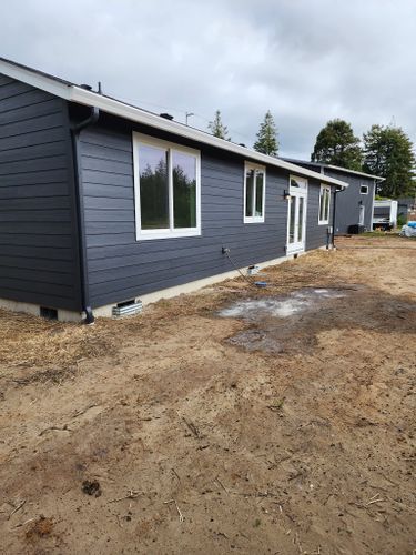 A black house with white windows is sitting in the middle of a dirt field.