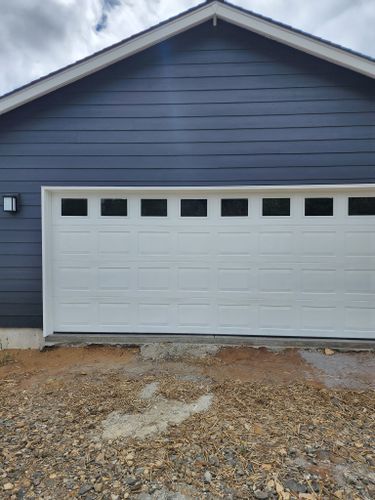 A white garage door is sitting in front of a blue house.