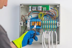 Gloved technician wiring a circuit panel with colorful cables and terminals