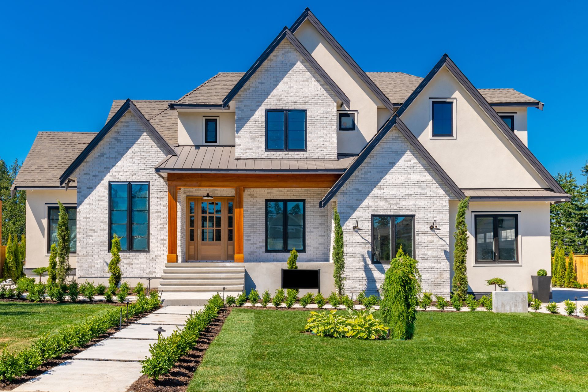 Two-story house with white brick exterior, dark windows, and manicured lawn.