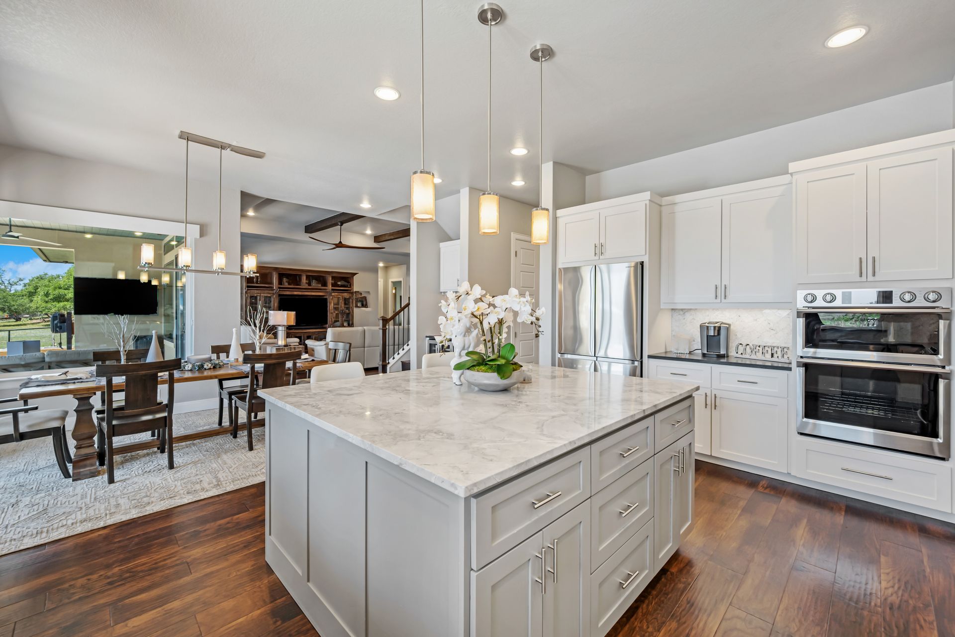 Modern kitchen with gray island, white cabinets, stainless steel appliances, and open layout to dining and living areas.