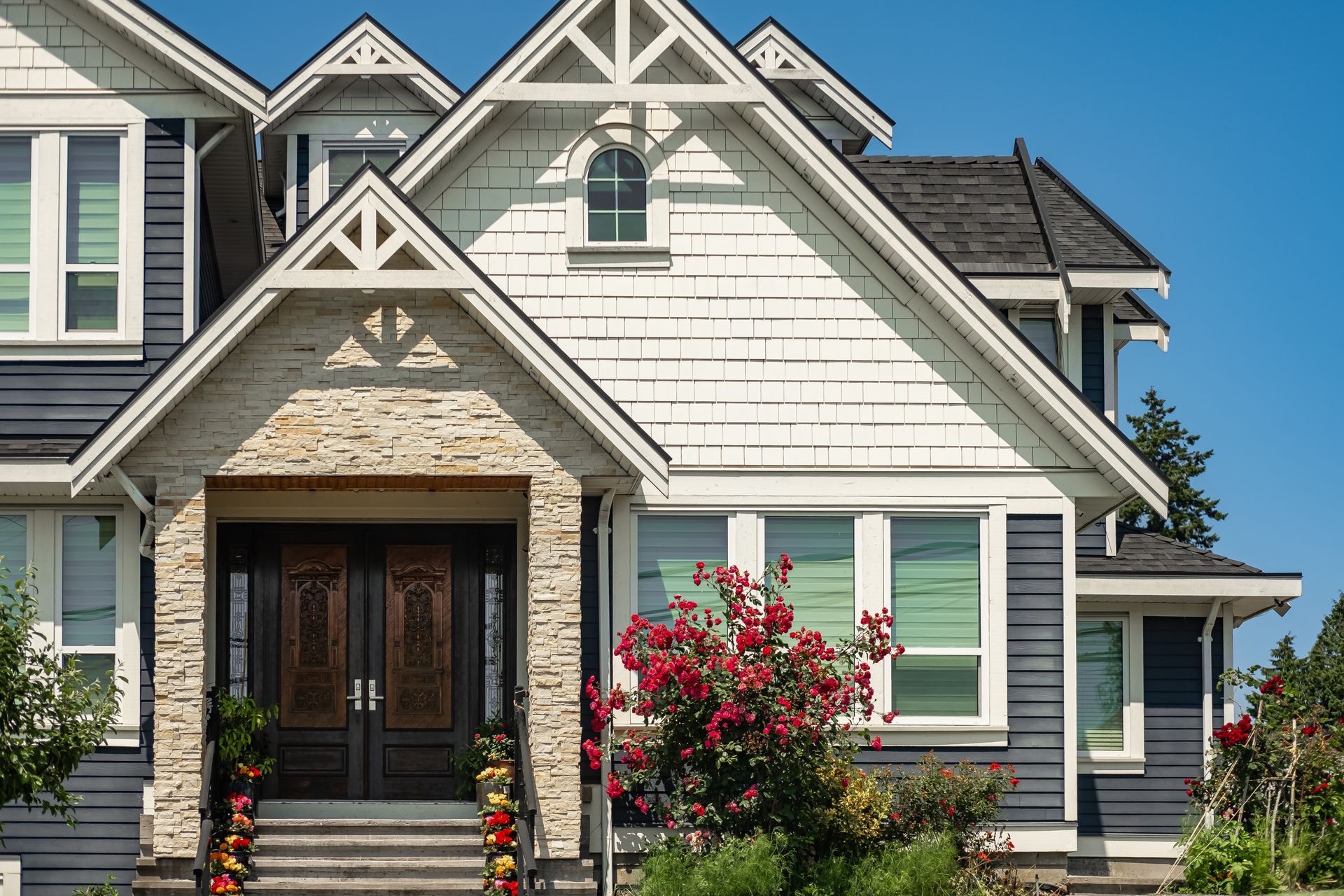 House exterior with blue siding, white trim, and stone entry. Red roses in front.