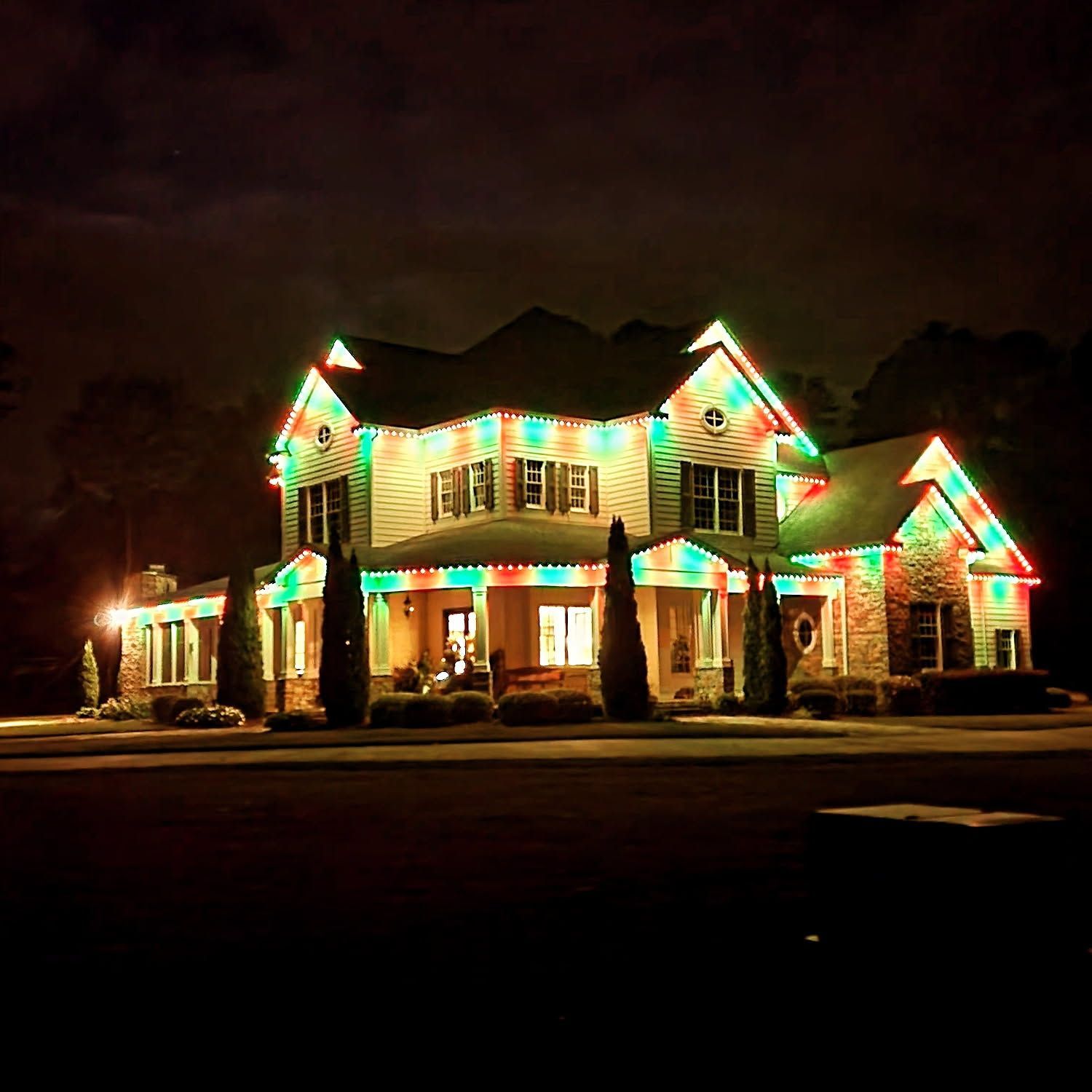 House lit with green and red Christmas lights at night.