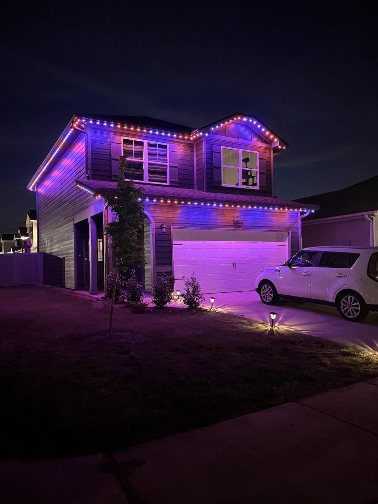 House lit up with purple and orange lights at night, car in driveway.
