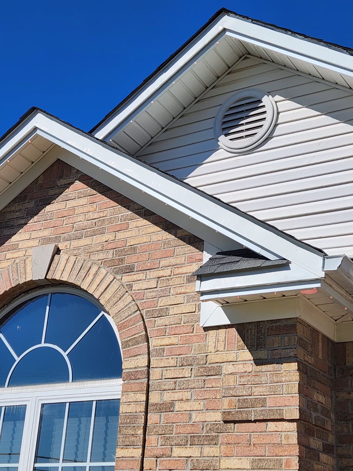 Brick house with arched window and white trim against a blue sky.