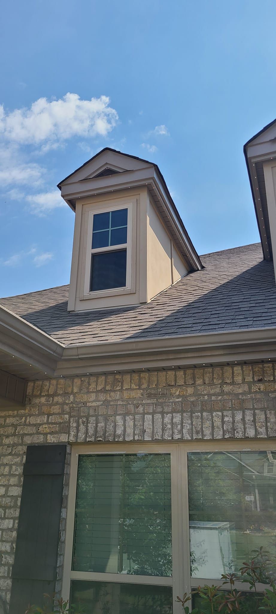 Dormer window on a brick house with tile roof against a blue sky.