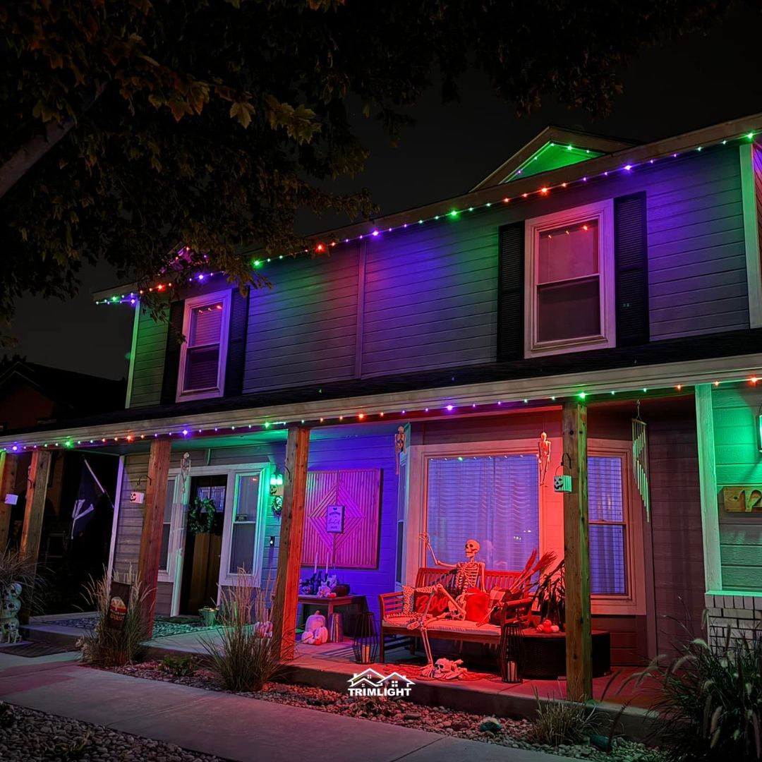 House decorated for Halloween with colorful lights. Porch has seating and a spooky ambiance.