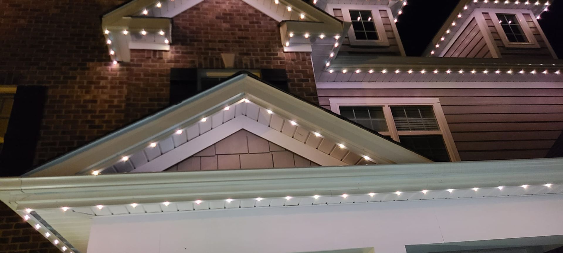 House exterior lit up with white lights along rooflines and gables at night.