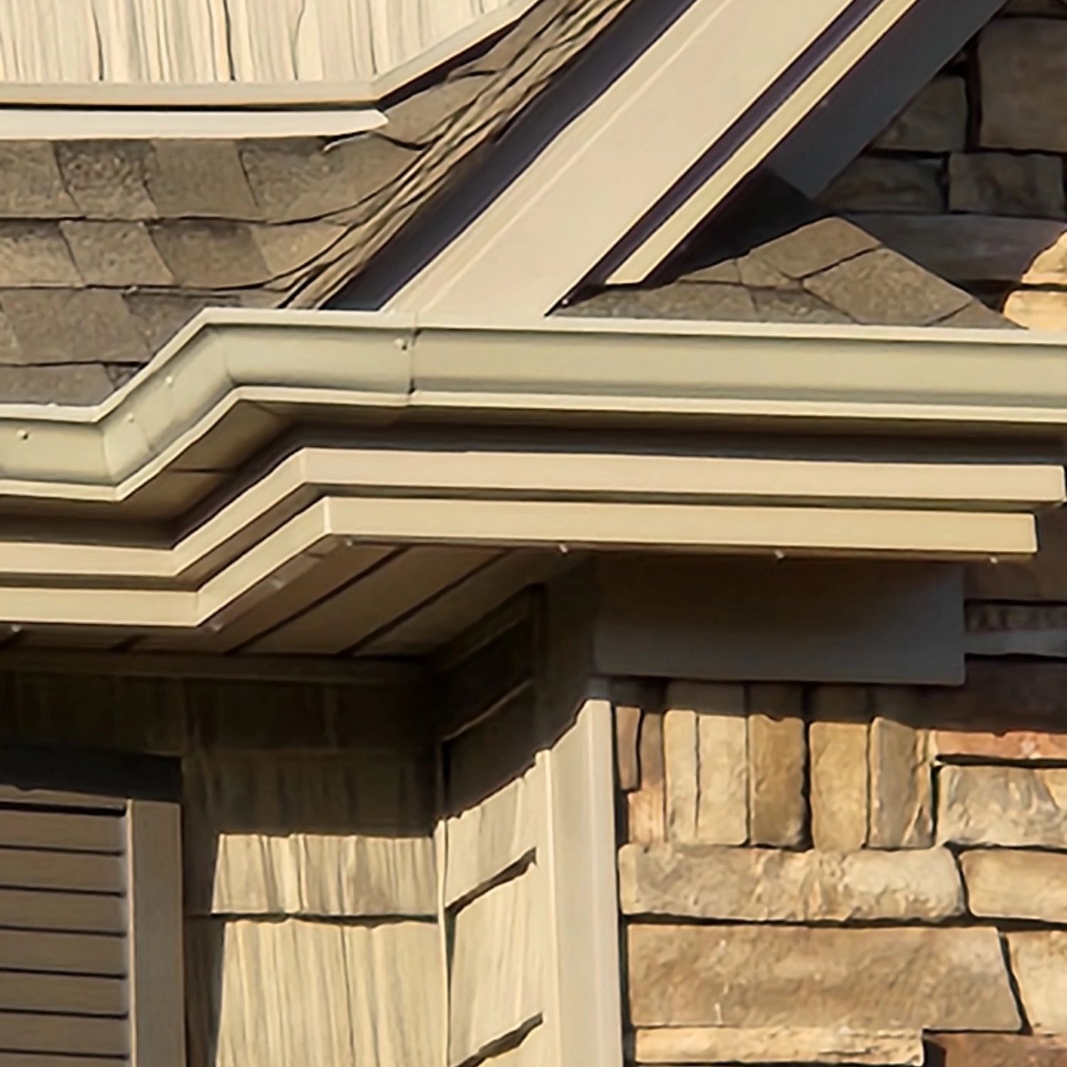 Beige gutters and trim on a house with stone and shingle siding.