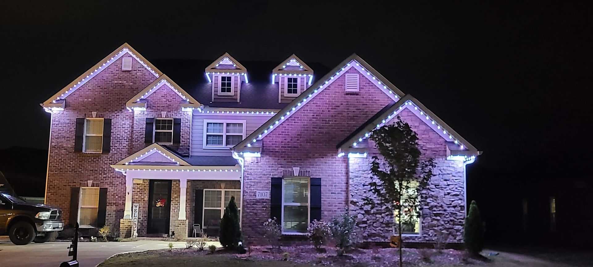 A brick house at night lit with purple lights for the holidays.