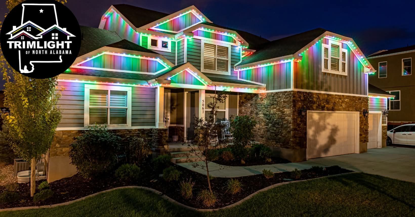 House with multi-colored LED lights outlining the roof and windows. Dark blue sky with lit windows.