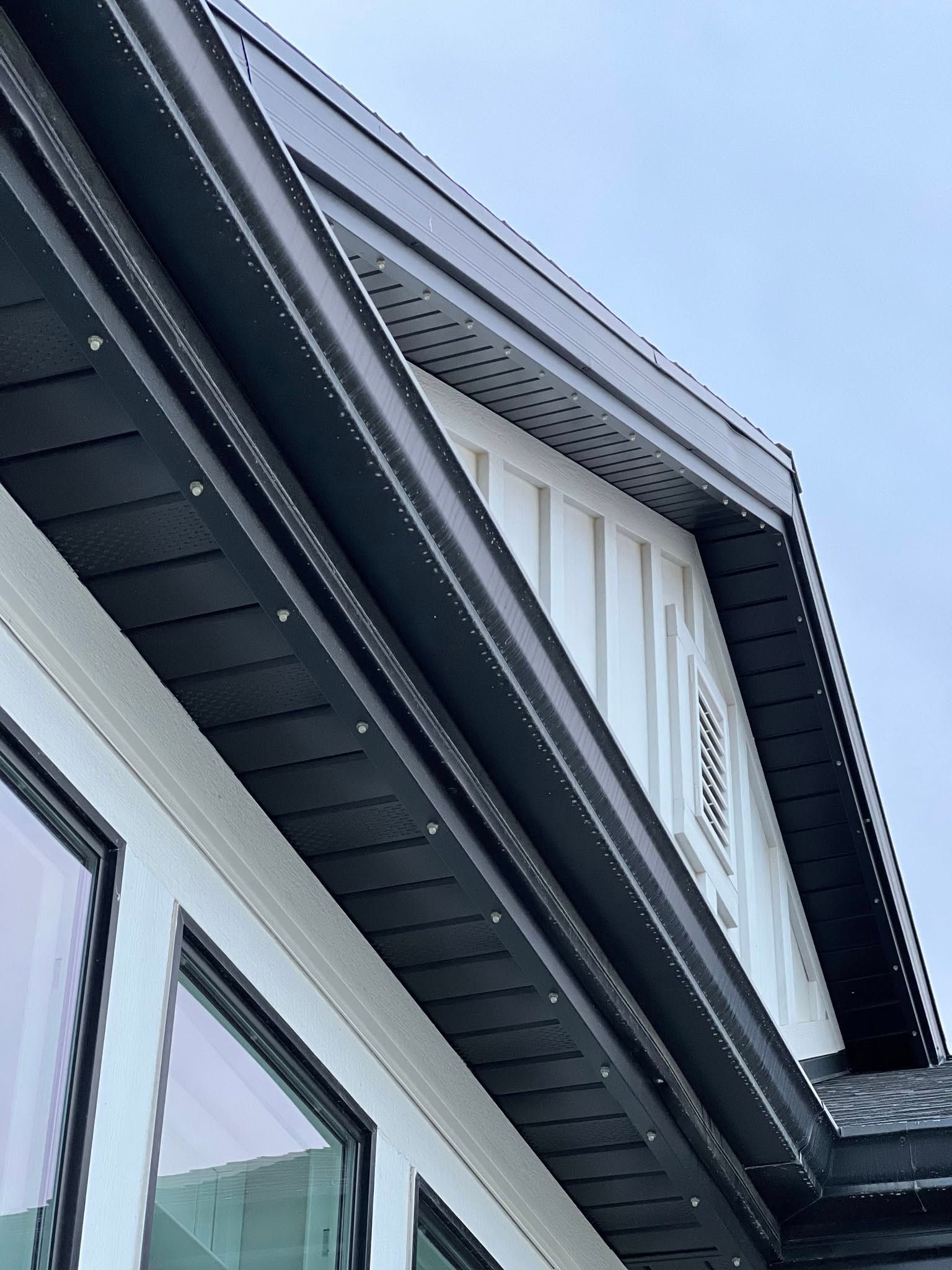 Black roof trim on a white house, with a dark gray soffit and a small window under the eaves.