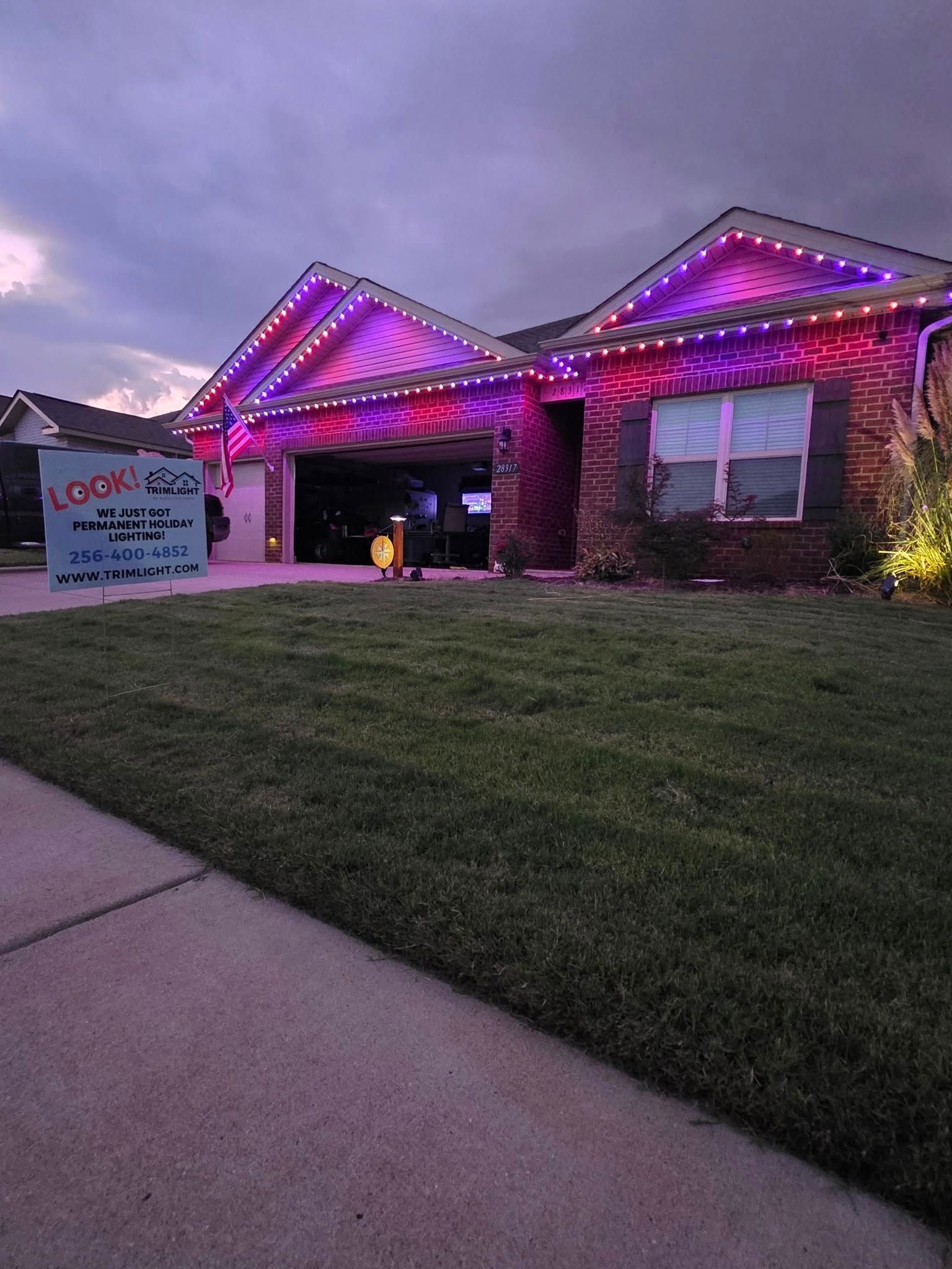 House with purple and pink lights on the roof and garage. Sign on the left, dark sky.