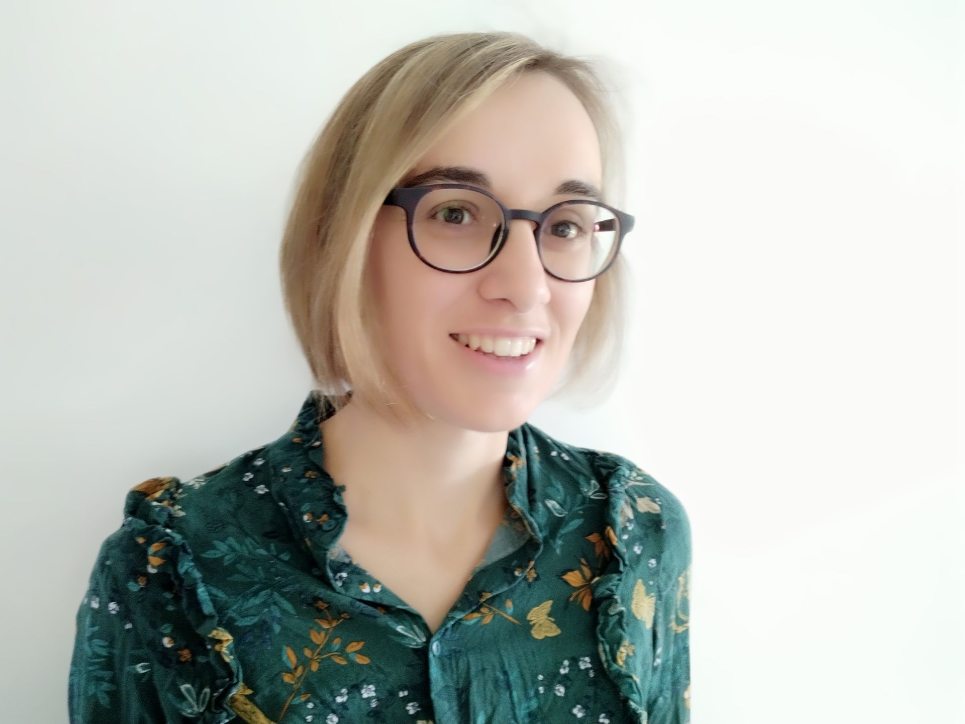 Une femme portant des lunettes et une chemise verte sourit.