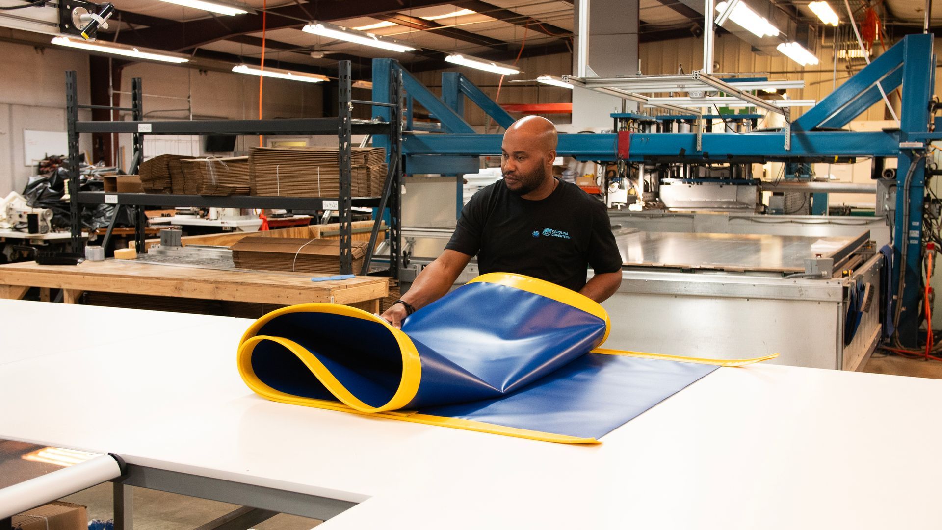 A man is laying a blue and yellow mat on a table in a factory.