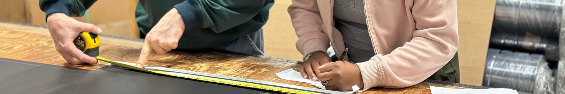 A man and a woman are measuring a piece of wood with a tape measure.