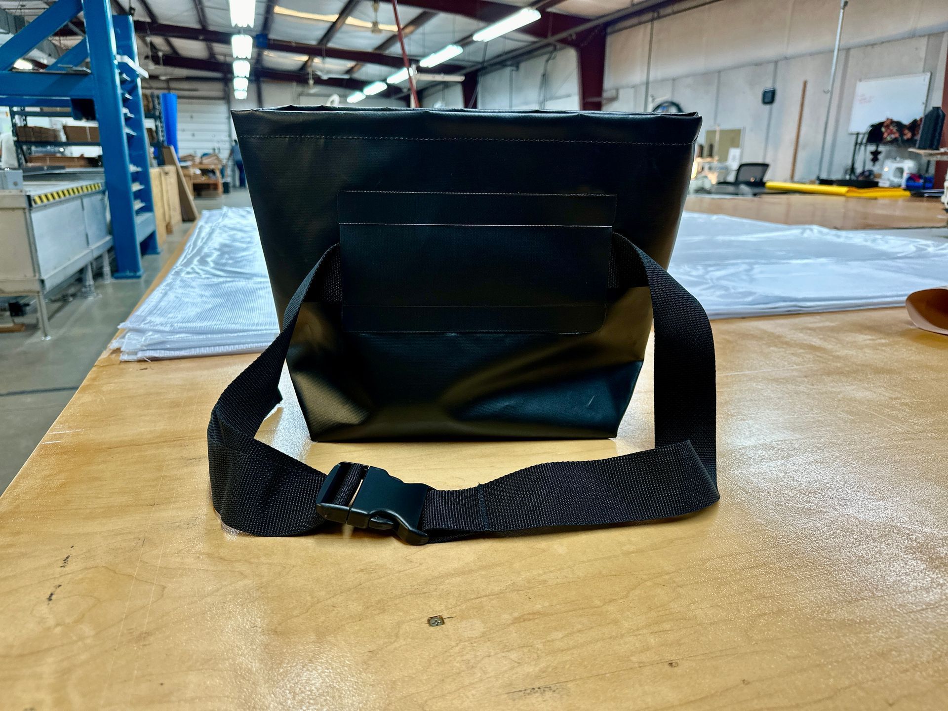 A black bag with a black strap is sitting on a wooden table.