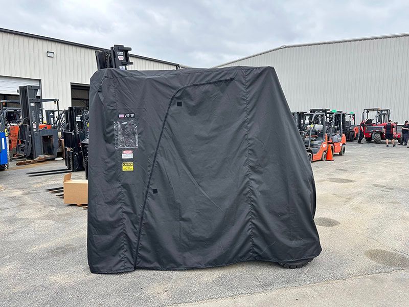 A black tarp is covering a forklift in a parking lot.