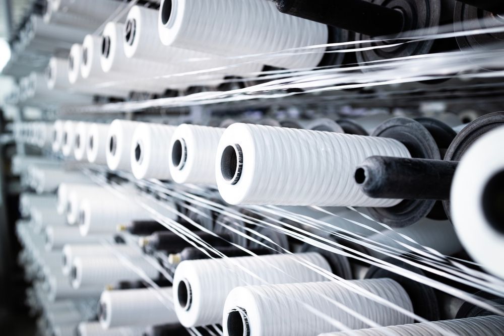 White spools of thread on a textile machine, with threads stretching across the frame.