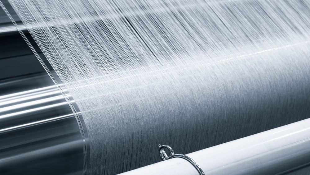 Close-up of a textile weaving machine with white threads being interlaced, creating fabric.