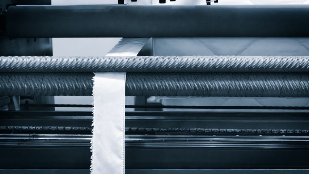Close-up of industrial machinery; a white ribbon is being fed through rollers.