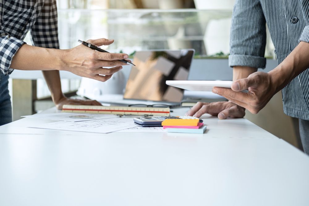 Two people collaborating at a desk, one points with a pen, the other holds a tablet.