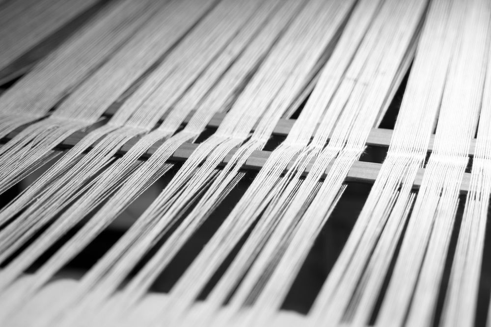 A black and white photo of a loom with white yarn.