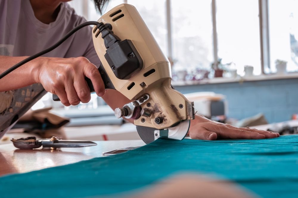 A person is cutting a piece of fabric with a machine.