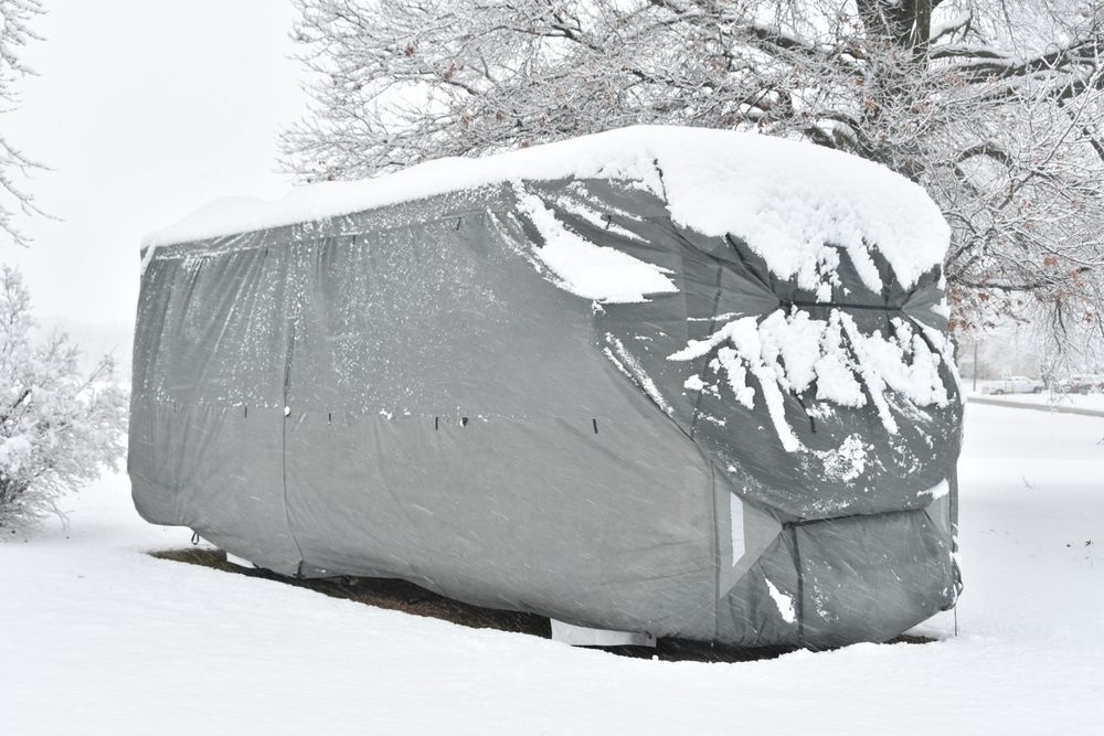 A rv with a cover on it is covered in snow.