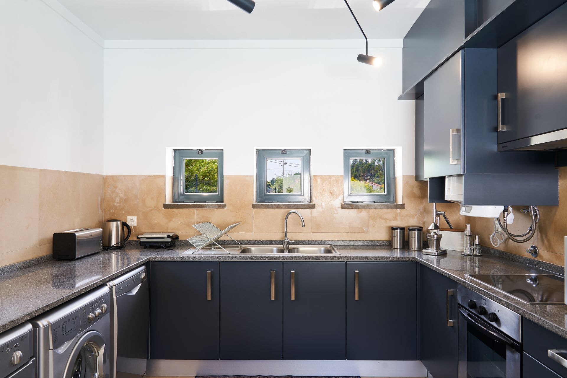 Modern kitchen with dark blue cabinets, granite countertops, and three small windows.
