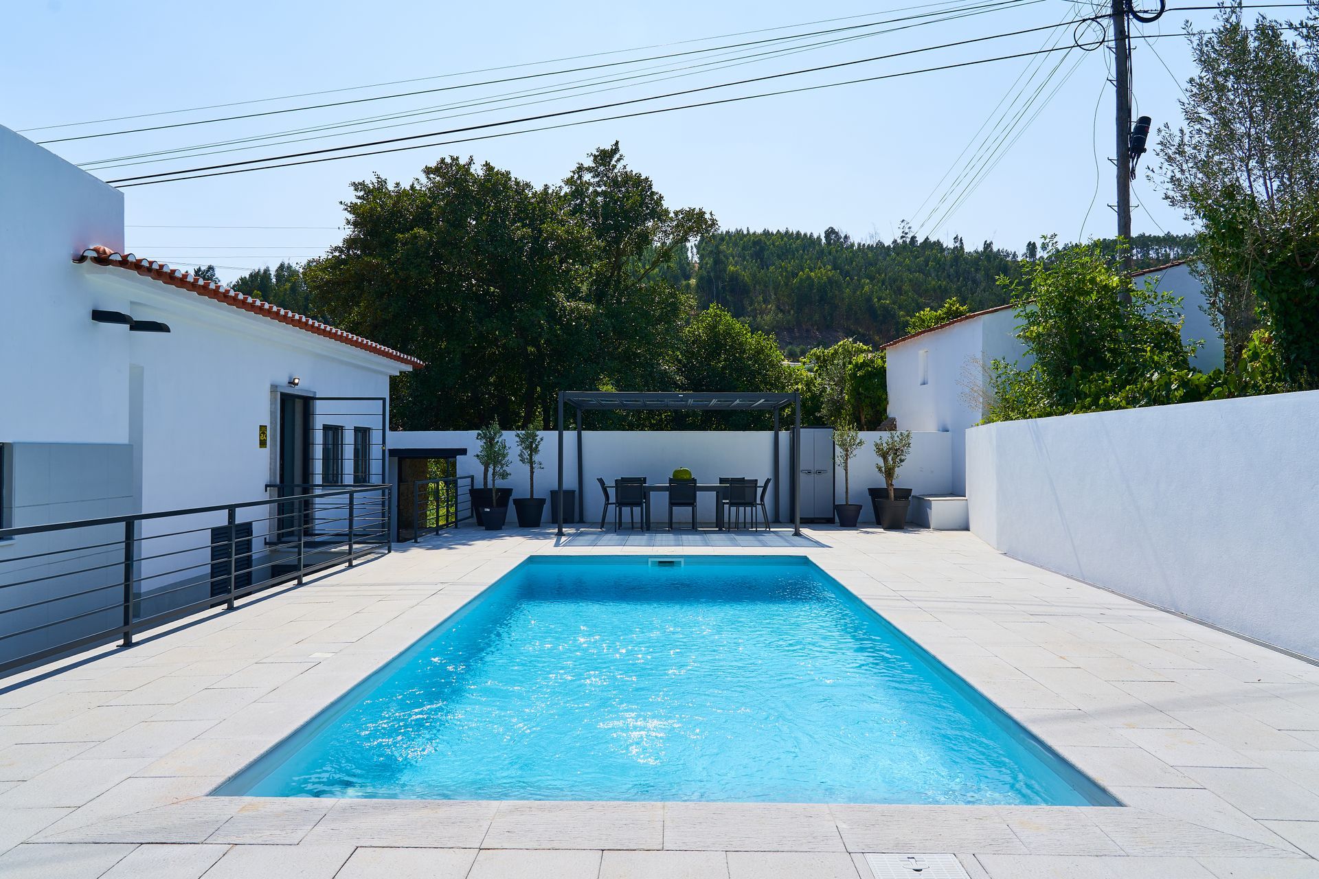 Rectangular swimming pool in a white-walled yard, with seating area under a pergola.